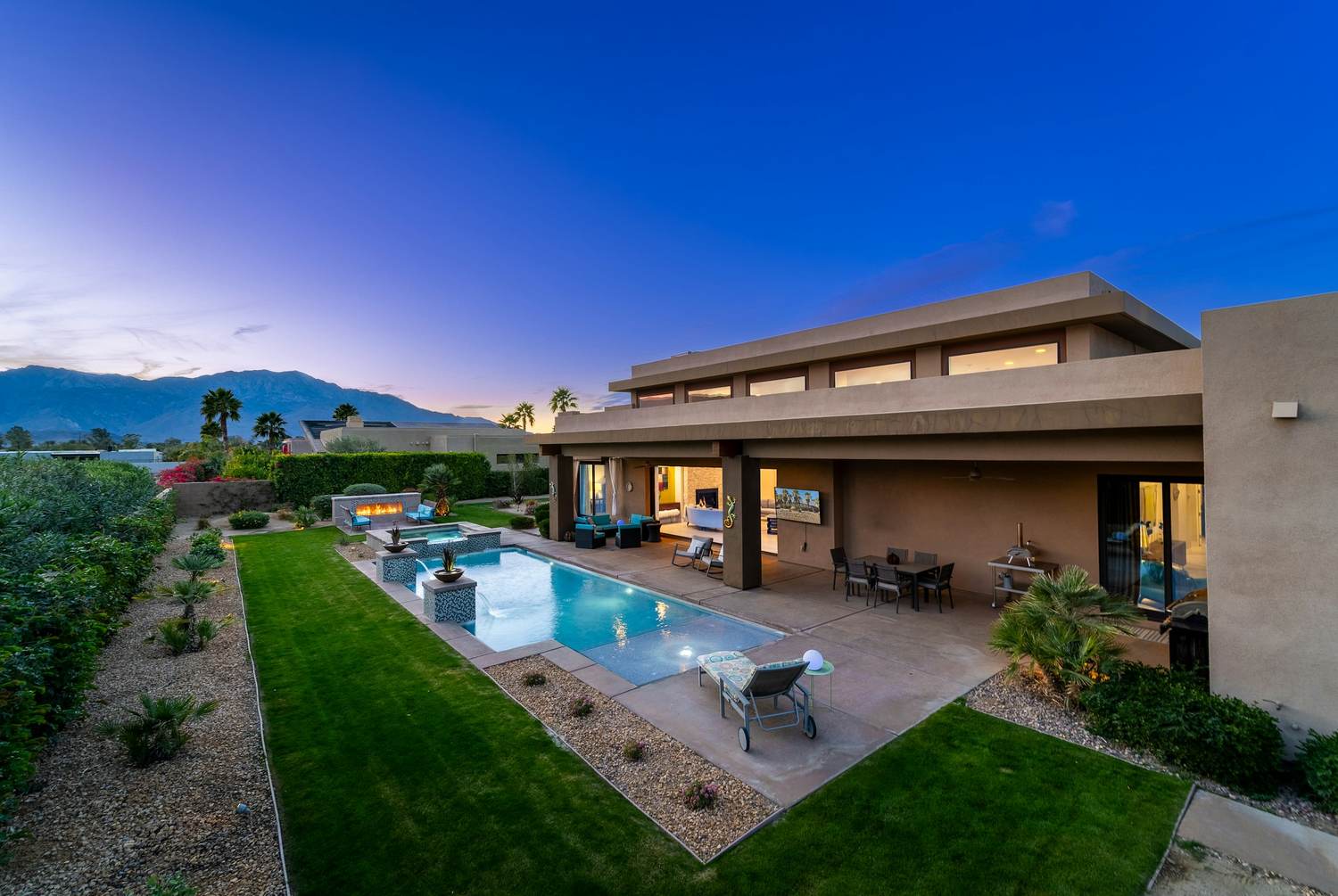A desert home and pool lit at dusk, mountains behind